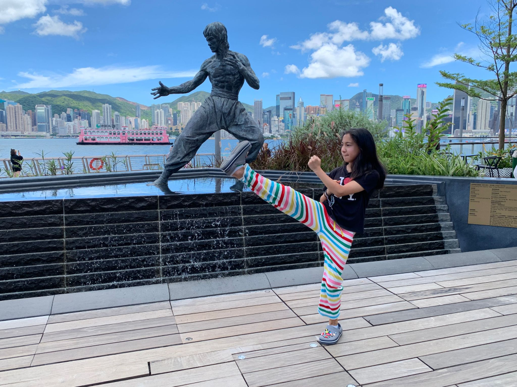 Mia practicing high kick by a Bruce Lee statue in Hong Kong